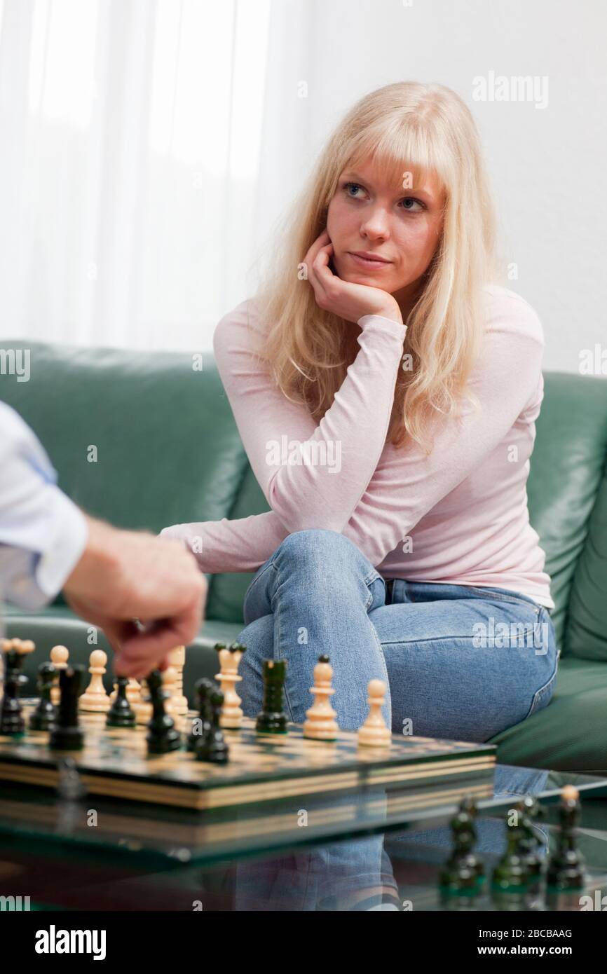 Jeune femme pensive jouant aux échecs avec son partenaire notre père à la maison Banque D'Images