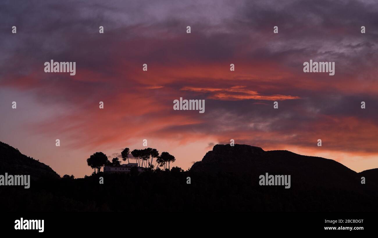 Silhouette d'une villa au sommet d'une colline avec un fond de ciel de coucher de soleil coloré étonnant, nuages dans des tons doux orange et rose Banque D'Images