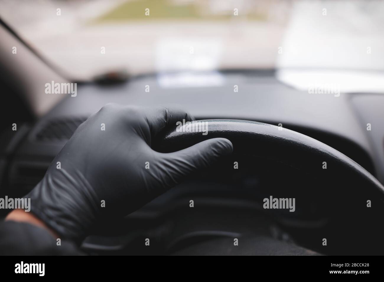 Détails avec la main d'un conducteur, dans un gant en latex, sur un volant noir pendant la pandémie de Covid-19. Banque D'Images