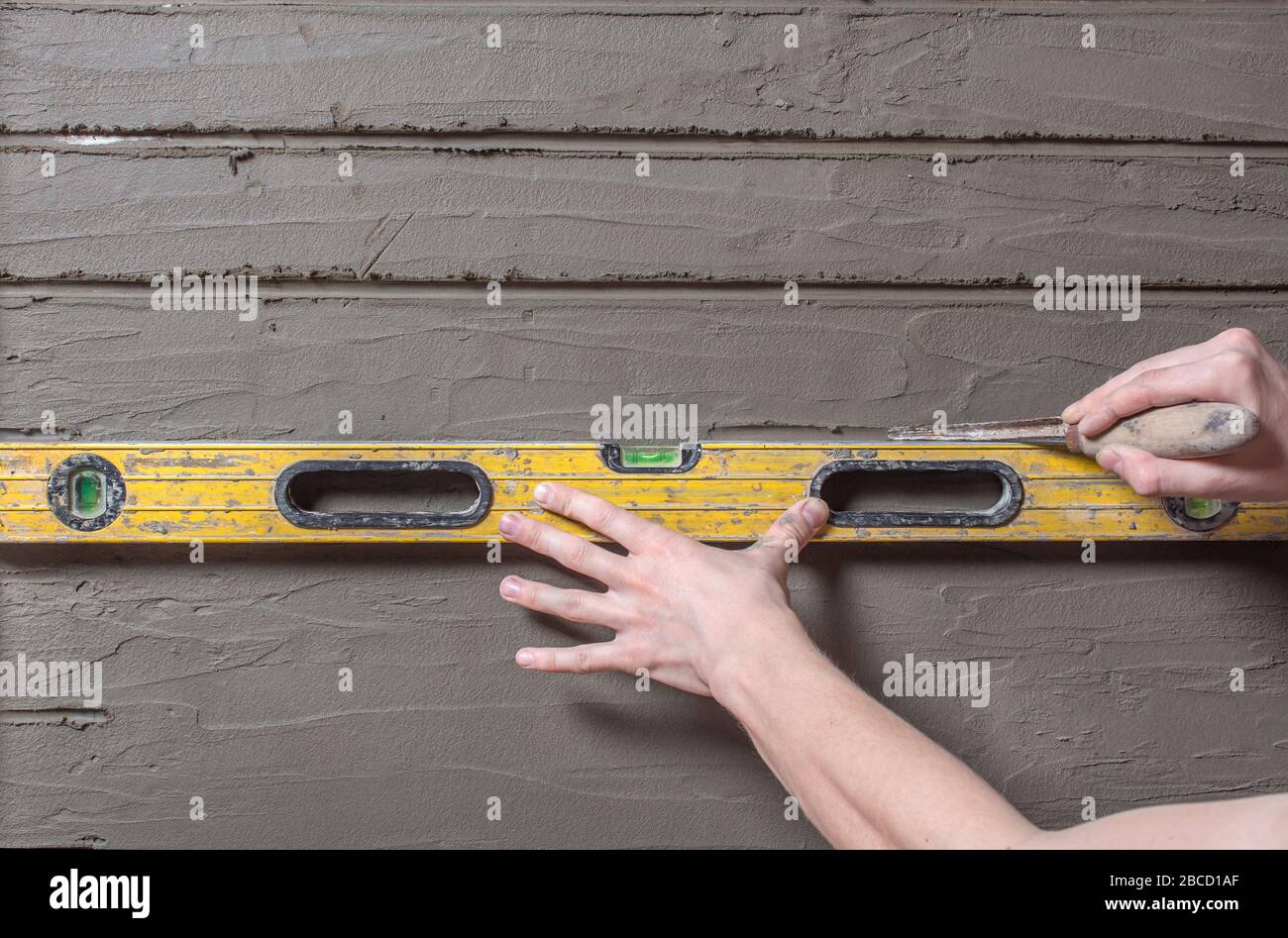 Le constructeur maintient le niveau de construction et marque le mur. La main dessine des bandes horizontales de broderie sur le plâtre. Réparation de murs dans le ho Banque D'Images