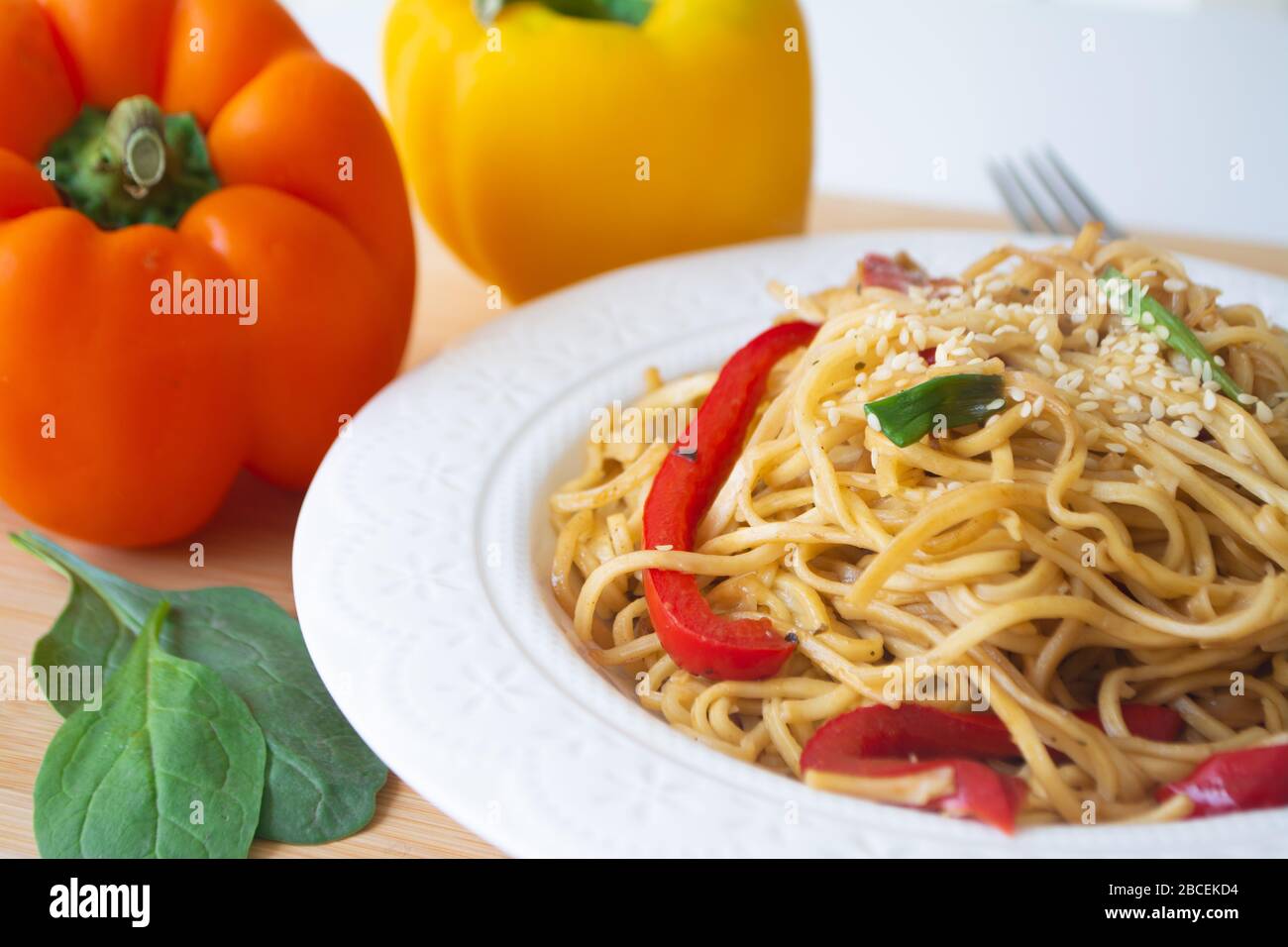 Nouilles chinoises aux œufs dans la sauce soja avec poivrons colorés, légumes verts et oignons printaniers avec graines de sésame saupoudrées sur le dessus Banque D'Images