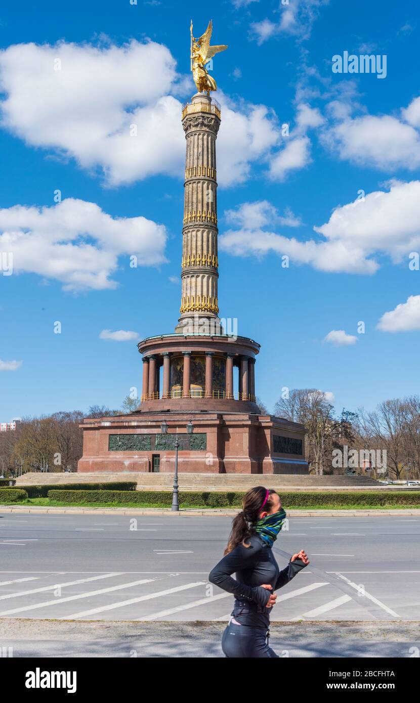 Jogger couvrant son visage passant devant Siegessaeule Victory Column dans le parc Tiergarten dans le centre de Berlin pendant le verrouillage de la pandémie de couronne Banque D'Images