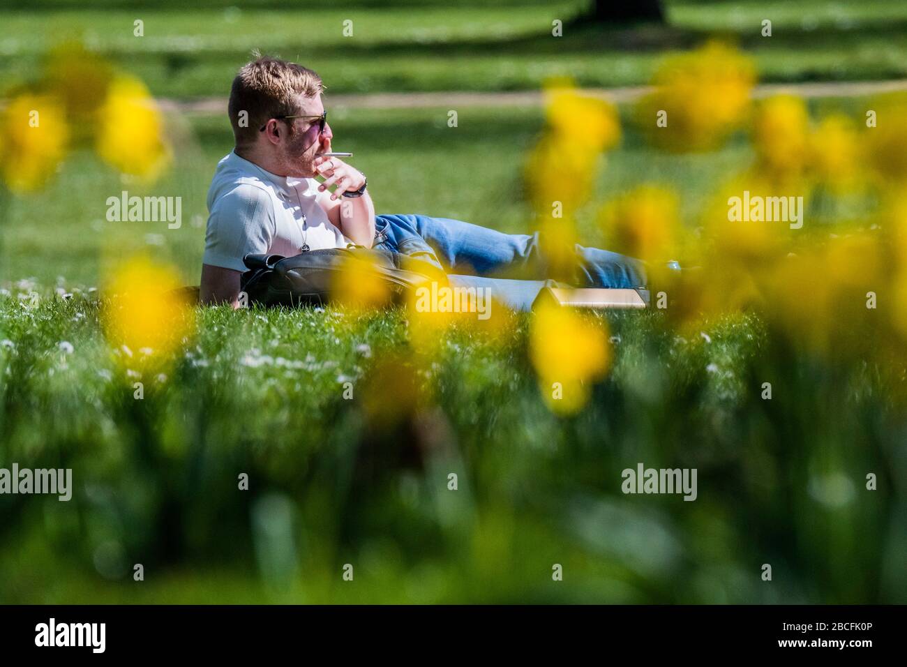 Londres, Royaume-Uni. 4 avril 2020. Un homme se trouve en bas pour une cigarette, ignorant les conseils du gouvernement et profiter du soleil dans Green Park - une journée ensoleillée et les gens sont dans un nombre raisonnable, dans tout Londres, pour faire leur exercice quotidien. Le « verrouillage » se poursuit pour l'épidémie de Coronavirus (Covid 19) à Londres. Crédit: Guy Bell/Alay Live News Banque D'Images