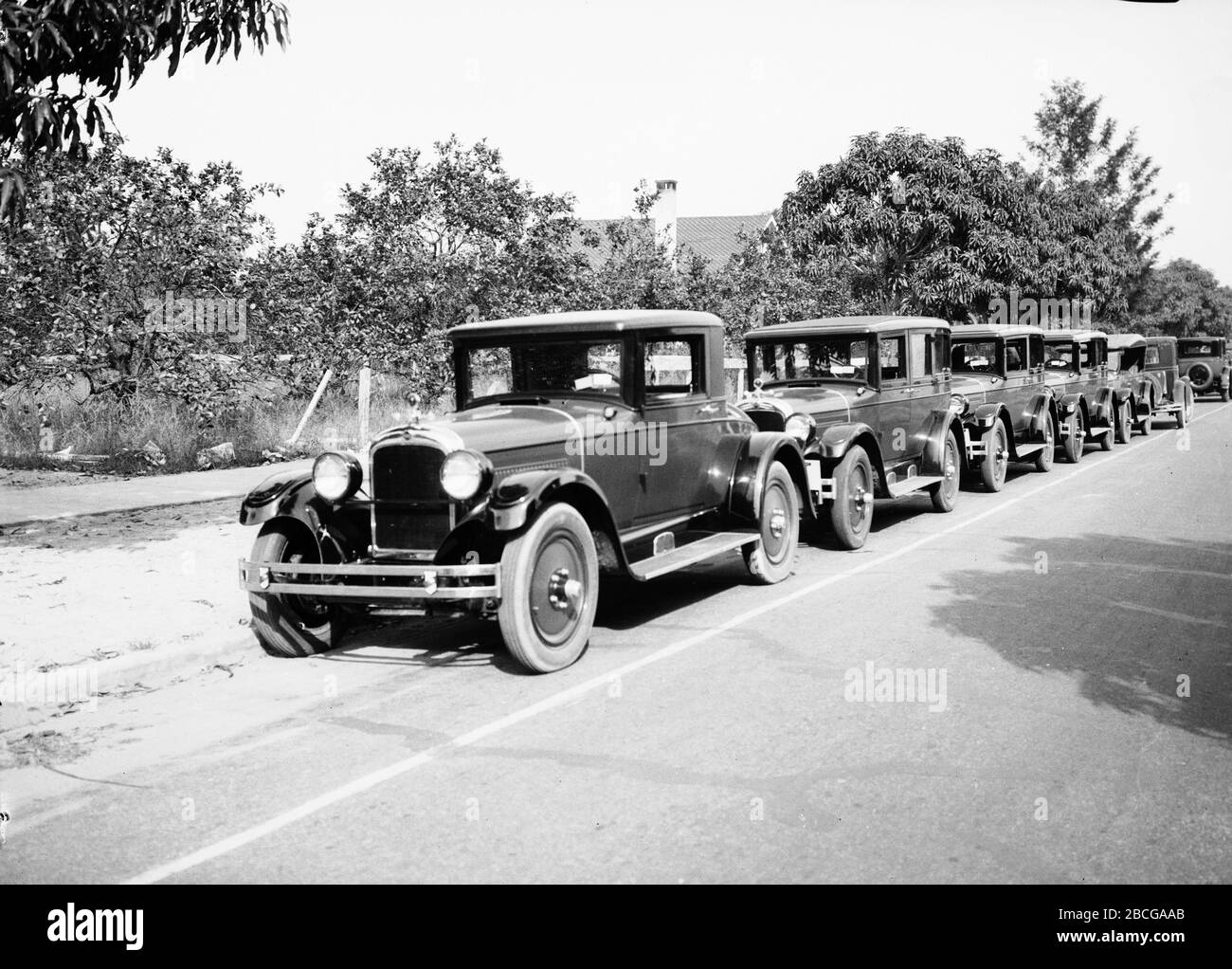 Une ligne de voitures garées le long d'une rue, années 1920. Photographie par Burton Holmes. Banque D'Images