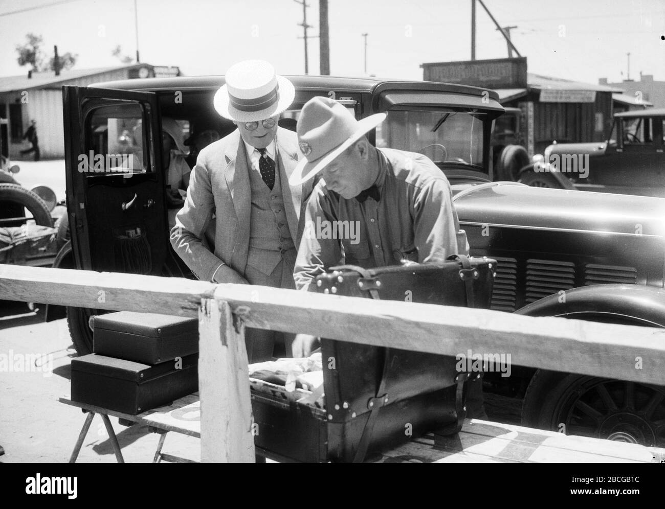 Un inspecteur américain des douanes examine les bagages appartenant à un homme à la frontière entre les États-Unis et le Mexique à Tijuana, au Mexique, et à San Ysidro, en Californie, dans les années 1920. Photographie par Burton Holmes. Banque D'Images