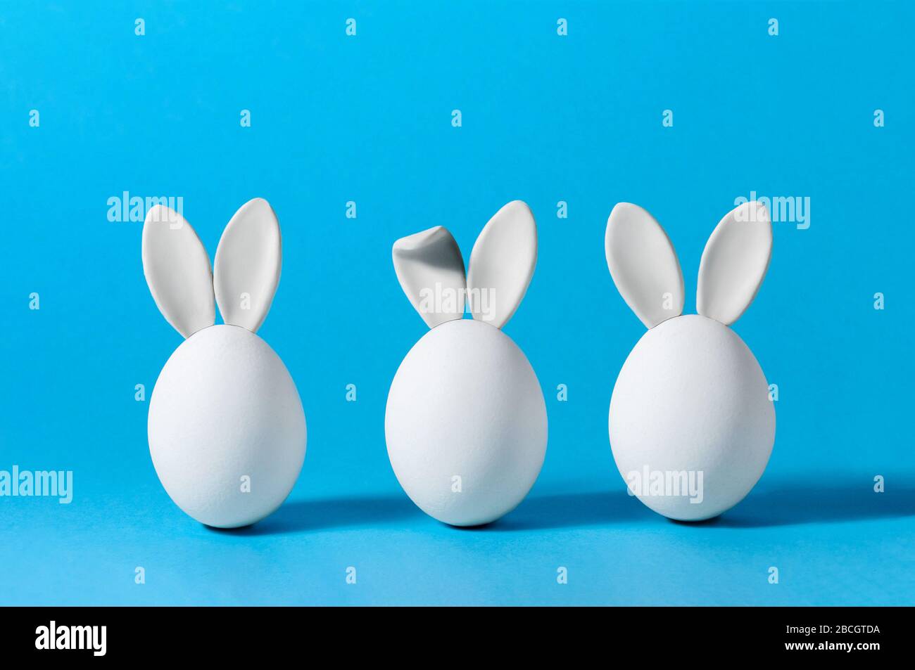 Œufs de Pâques avec oreilles de lapin sur fond bleu. Carte de vœux créative. Concept de minimalisme. Espace de copie pour votre texte Banque D'Images