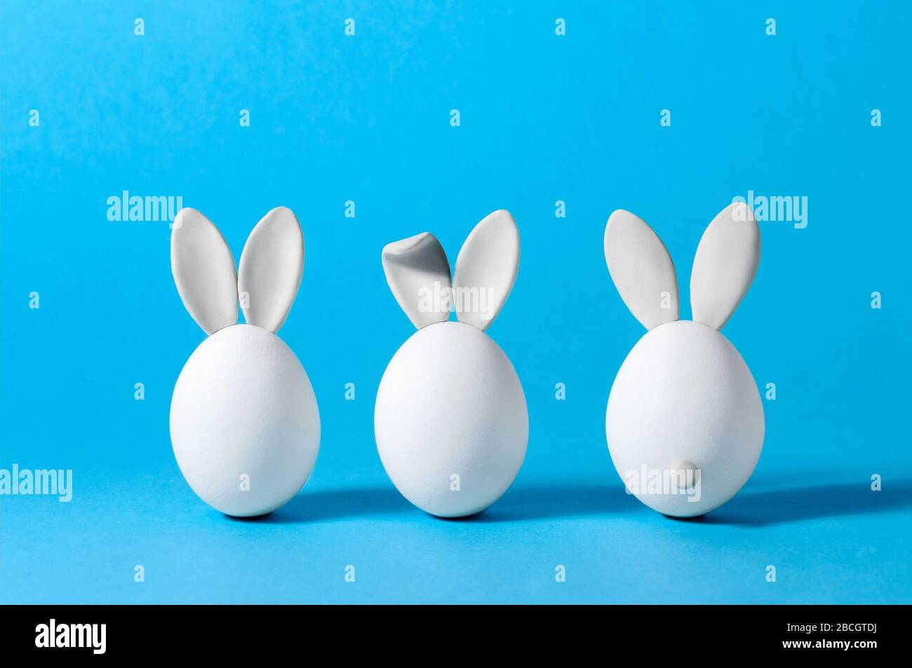 Œufs de Pâques avec oreilles de lapin sur fond bleu. Carte de vœux créative. Concept de minimalisme. Espace de copie pour votre texte Banque D'Images