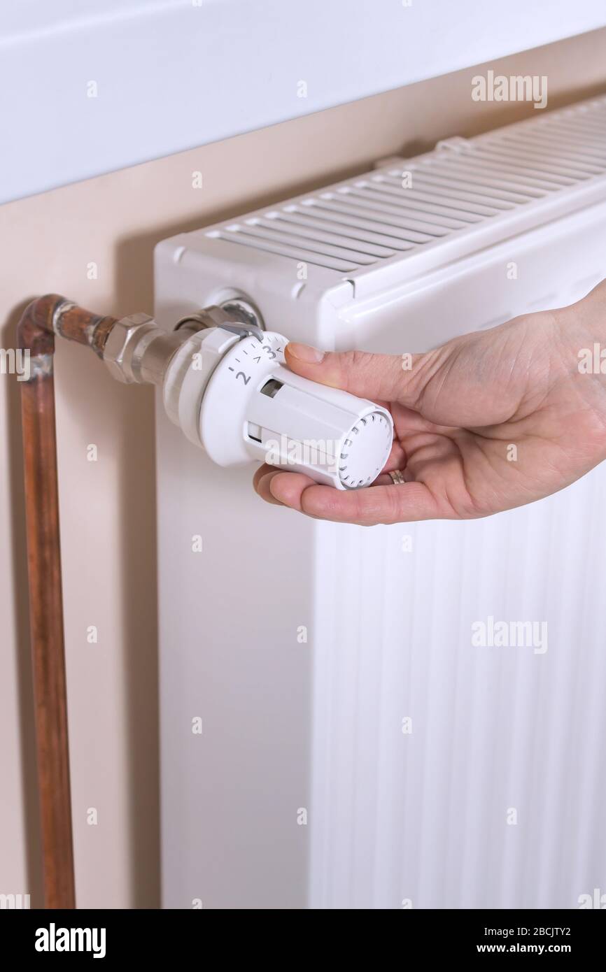 La main de la femme maintient le distributeur de température du radiateur et définit la valeur requise. Radiateur blanc et tuyaux d'eau en cuivre sur le second backgro Banque D'Images