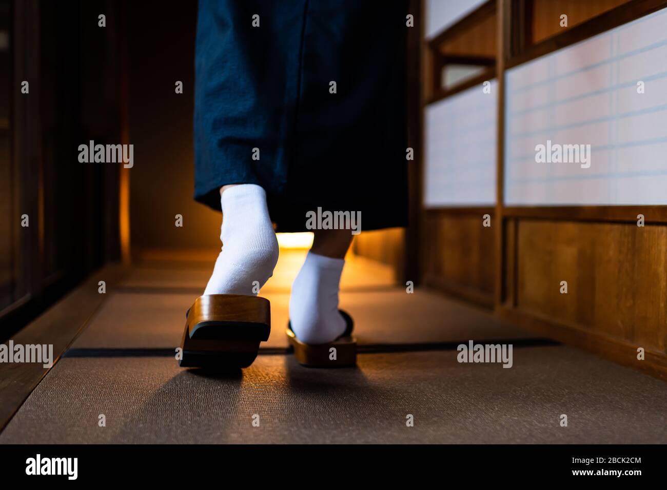Maison traditionnelle de ryokan japonais avec homme dans kimono dos closeup de pieds de jambes avec des chaussettes blanches de tabi et des chaussures de geta marchant par le doo de papier glissant de shoji Banque D'Images