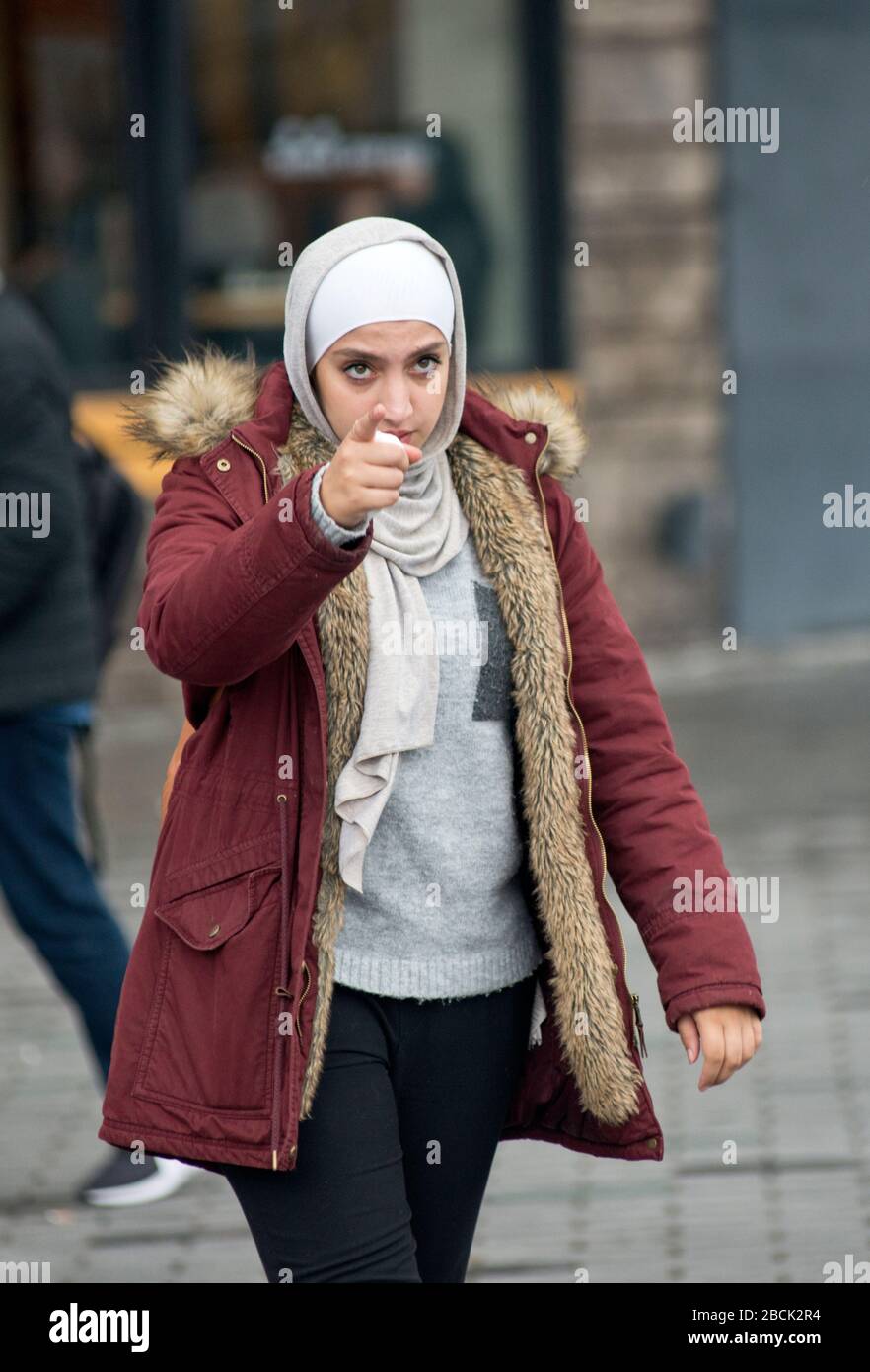 Une fille musulmane portant un pashmina et un manteau d'hiver, pointant avec son doigt. Place Taksim, Istanbul. Turquie Banque D'Images