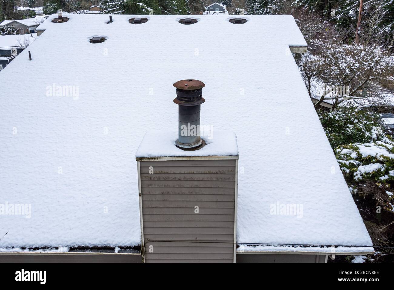 Toit de la maison recouvert de neige, cheminée rouillée, évents de toit, parement en bois Banque D'Images
