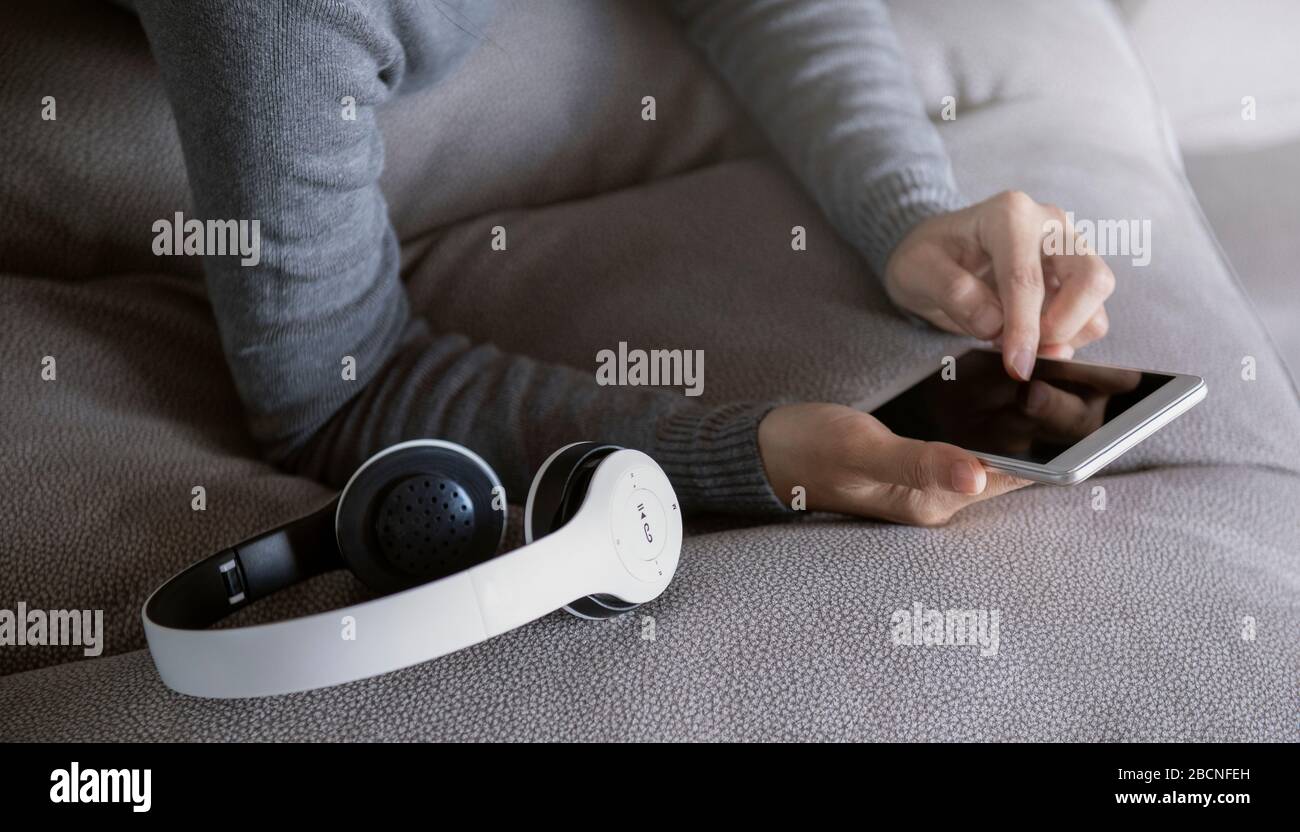 La femme est posée au téléphone sur le canapé avec des écouteurs de son côté. Rester à la maison campagne des médias sociaux pour la prévention du coronavirus. Banque D'Images