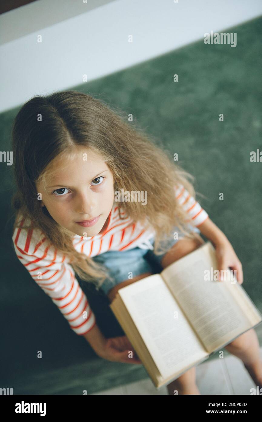 petite fille intelligente avec de longs cheveux assis sur un canapé vert avec livre sur son genou Banque D'Images