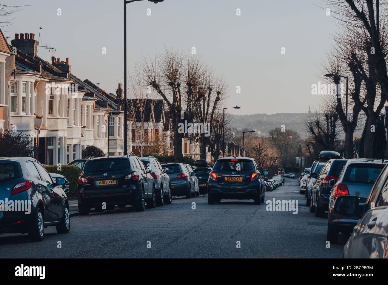 Londres, Royaume-Uni - 22 mars 2020: Voiture passe devant les voitures stationnées des deux côtés d'une rue à Palmers Green, une zone de banlieue du quartier londonien d'Enfield Banque D'Images