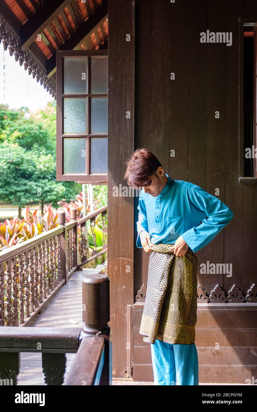 Malay homme portent un tissu traditionnel et ajuste son songket samping à la maison traditionnelle en bois. Banque D'Images