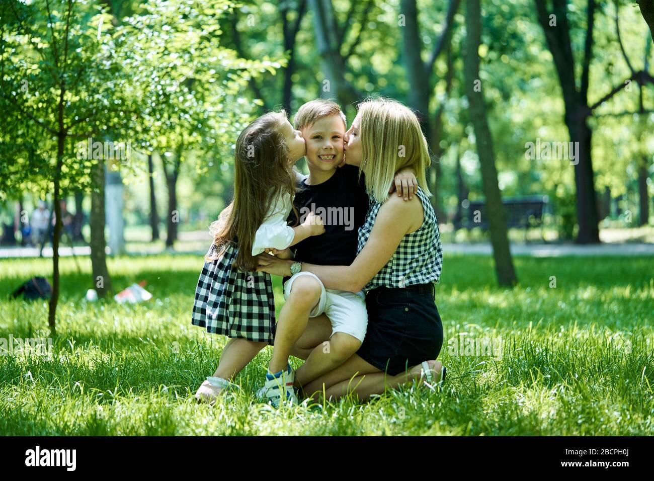 Bonne mère, fille et fils s'embrassant les uns les autres dans un parc. La mère et sa fille embrassent un petit garçon. Banque D'Images