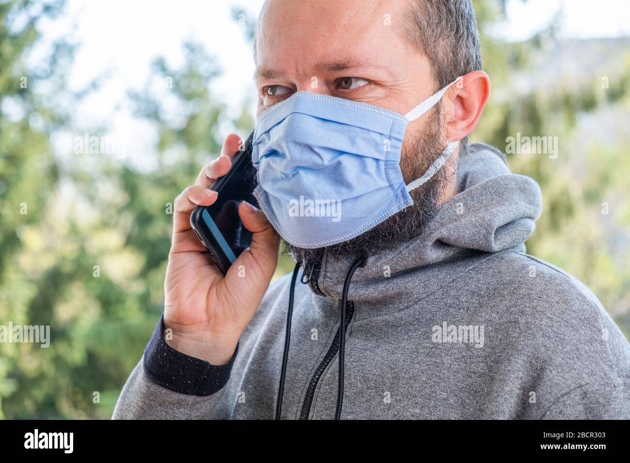 Gros plan d'un homme barbu avec une porotoection masque contre le coronavirus dans le parc, à l'aide d'un smartphone Banque D'Images