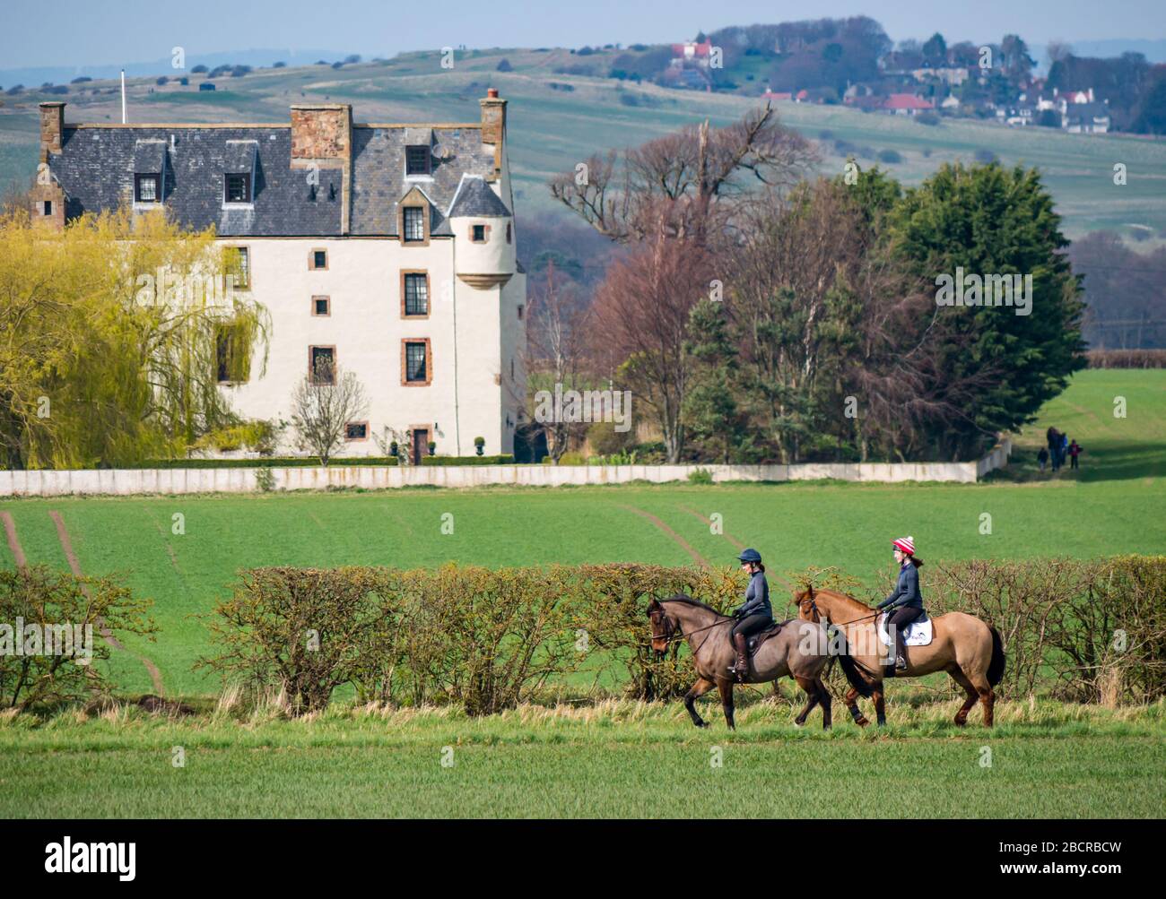 East Lothian, Écosse, Royaume-Uni. 5 avril 2020. Météo au Royaume-Uni : l'est du pays ressent enfin la chaleur du soleil de printemps car ceux qui vivent dans la zone rurale prennent leur exercice quotidien. Une femme et une fille s'exercent sur l'équitation, autour des bords des champs de récolte avec Ballencrieff House dans la distance Banque D'Images