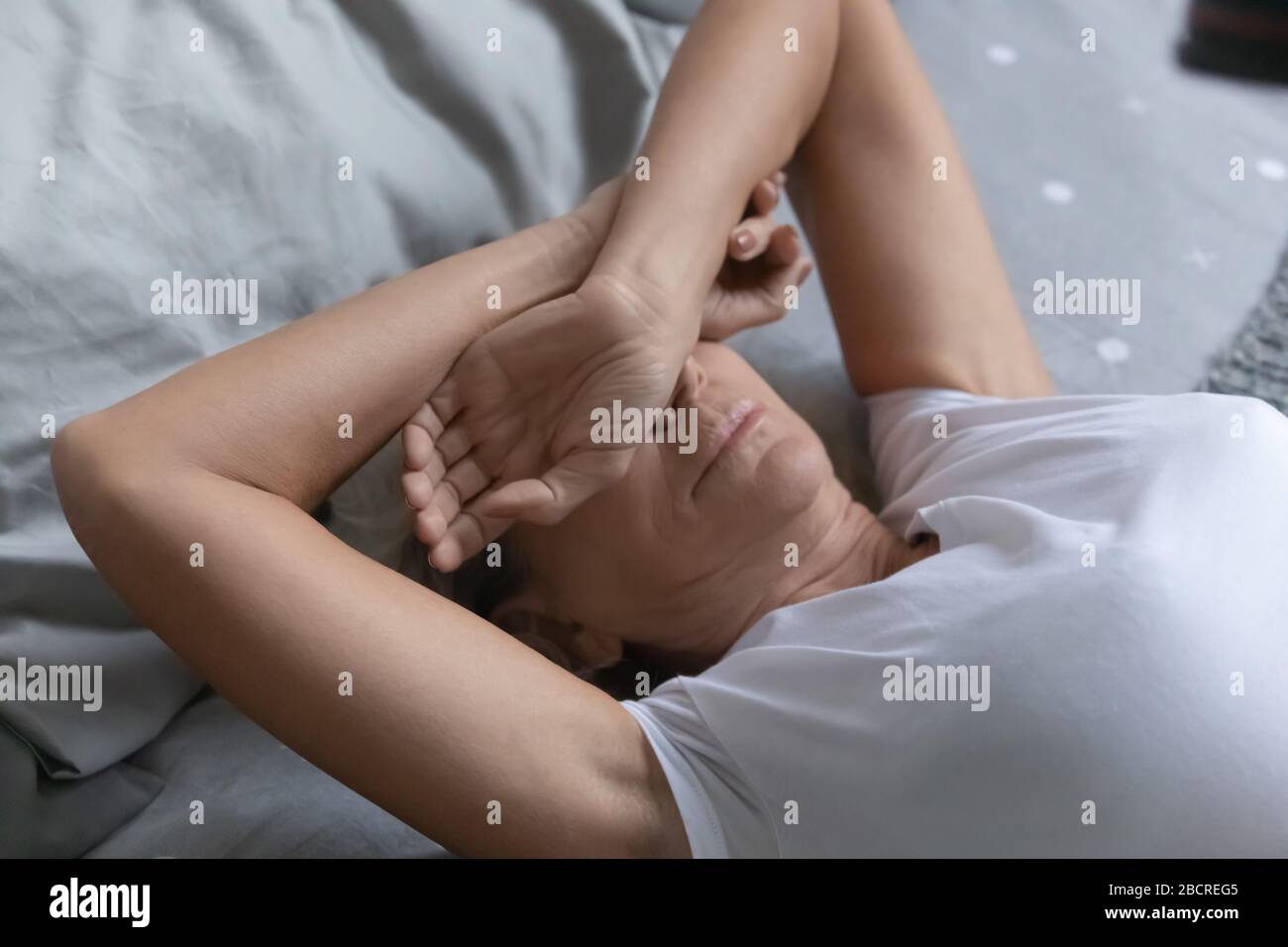Femme senior couvrant les yeux avec les bras, essayant de dormir dans la chambre. Banque D'Images