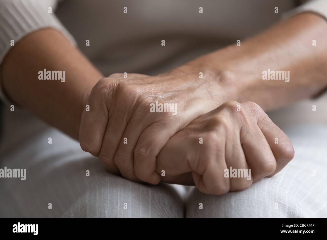 Femme senior d'âge moyen tenant des mains froissées sur les genoux. Banque D'Images
