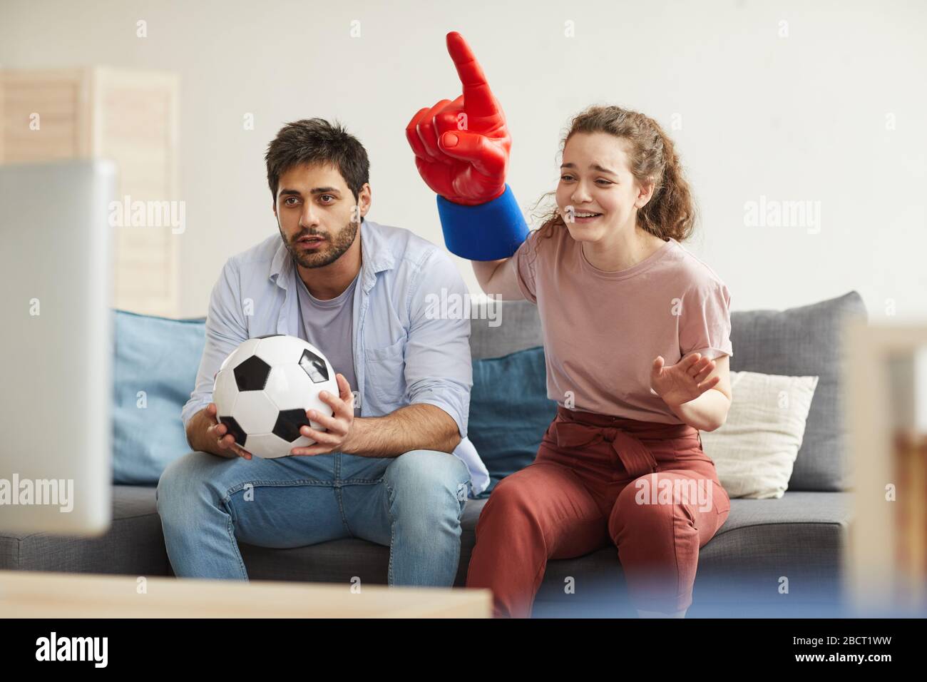 Couple de fans de sport enthousiastes regardant le match de football à la télévision à la maison et applaudisse émotionnellement, se concentrer sur la jeune femme portant un doigt de mousse, espace de copie Banque D'Images