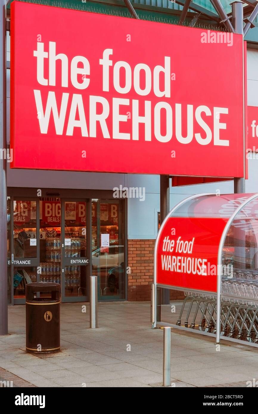 Entrée au supermarché, l'entrepôt de restauration montrant l'entrée et le logo de l'entreprise sur la signalisation et le parc de trolleys, Irvine Banque D'Images