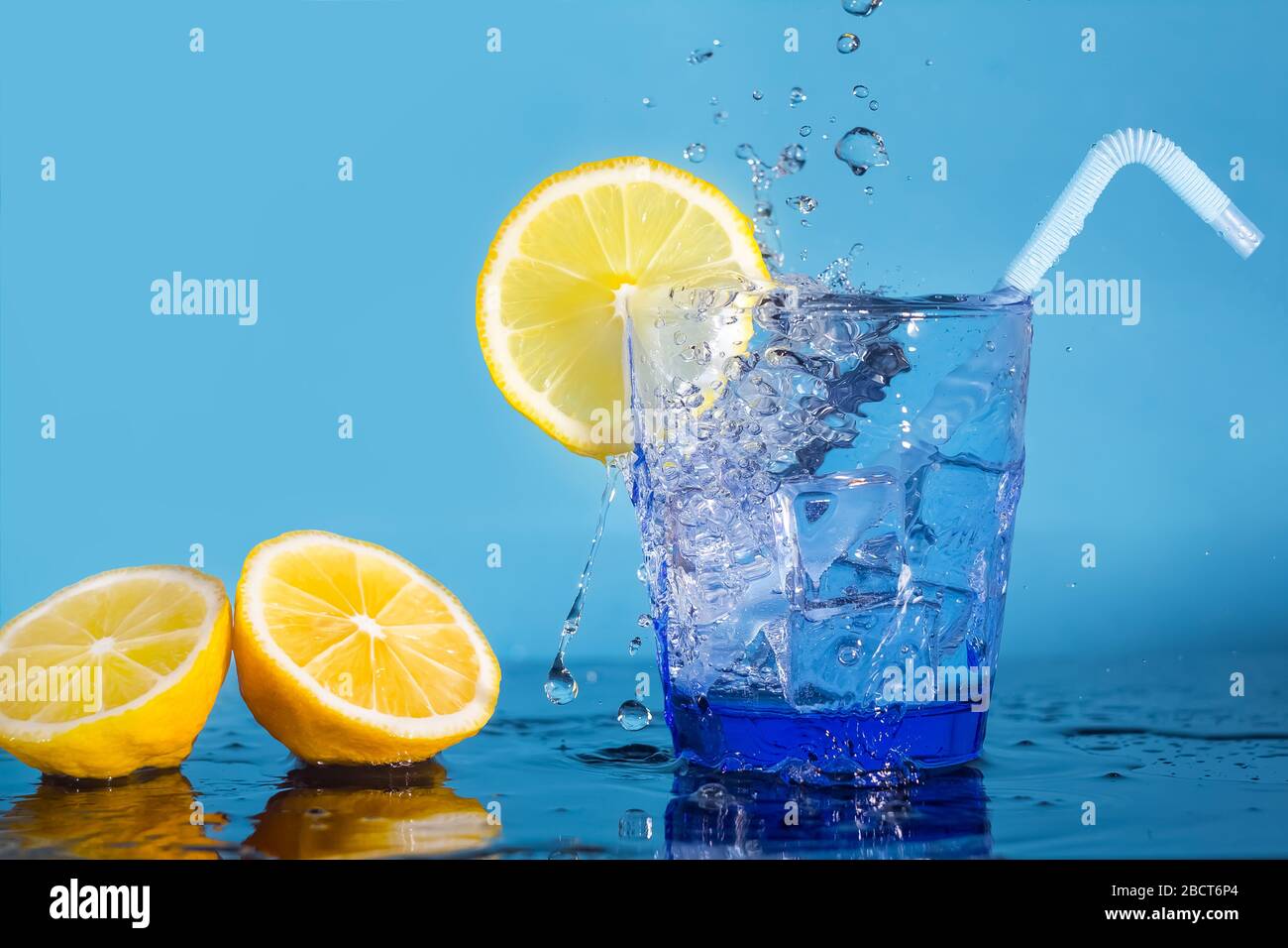 Un verre avec de l'eau et des glaçons, une tranche de citron frais, un tube et un jet d'eau qui tombe de dessus. Des gouttes d'eau tombent sur un citron frais. Un verre Banque D'Images