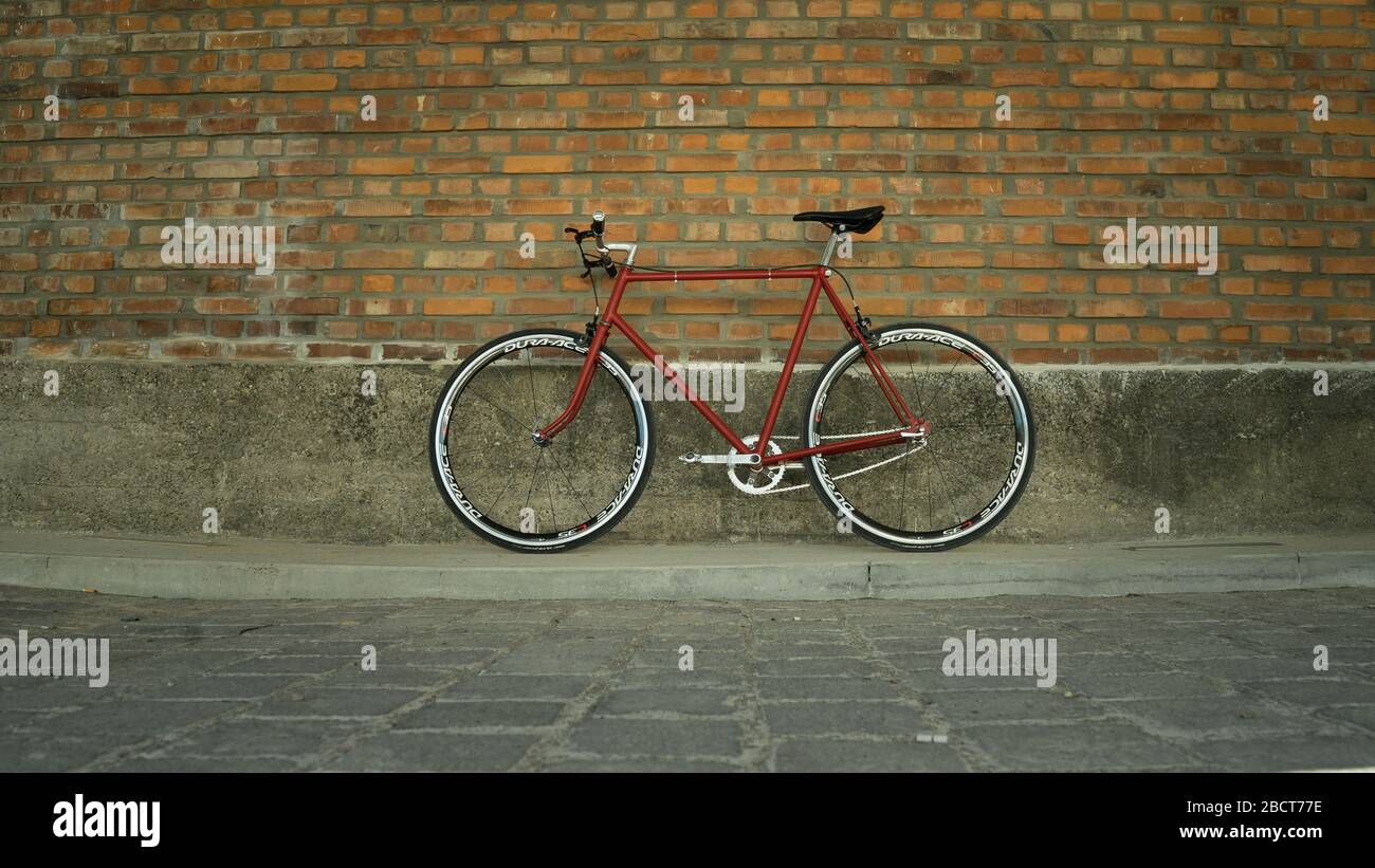 Vélo à engrenage fixe Singlespeed rouge de style rétro isolé sur un mur de briques Banque D'Images