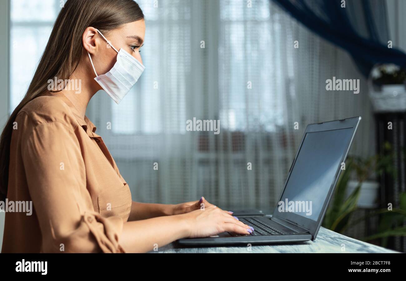 Femme portant un masque facial et travaillant sur un ordinateur portable, vue latérale Banque D'Images