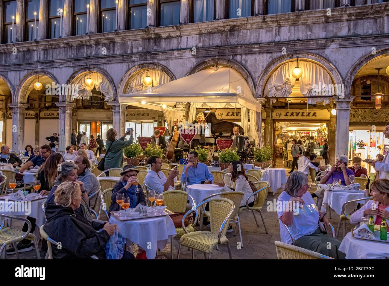 Les personnes assis à l'extérieur du Caffè Lavena sur la place St Marc en début de soirée à l'écoute du groupe de musiciens, Venise, Italie Banque D'Images