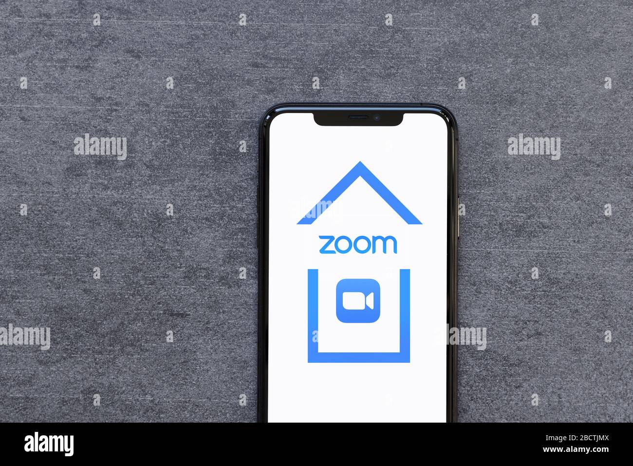 Smartphone avec logo de l'application Zoom à l'intérieur de la maison travailler à distance à partir de la maison quarantaine ou Lockdown concept sur fond de pierre naturelle. Banque D'Images