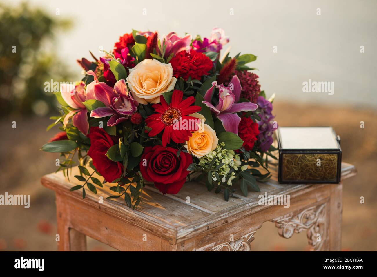 Table en bois de réception de mariage avec boîte pour la composition en anneau et en fleur avec roses rouges et pastel et orchidées roses à l'extérieur. Banque D'Images