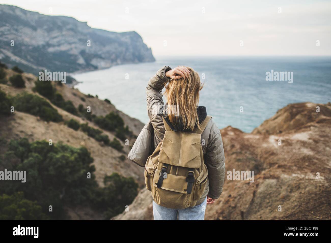 Backpacker hippie femme heureux de profiter d'une vue imprenable sur la mer  et la montagne depuis la colline. Vue de derrière. Concept de voyage.  Personne non reconnaissable dans un Jean et un