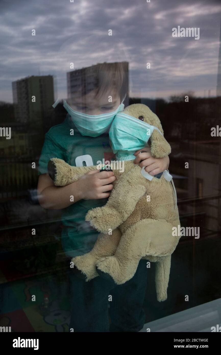 Coronavirus, Covid-19, Boy et son chiot farci dans des masques de protection regarder par la fenêtre, quarantaine à la maison Banque D'Images