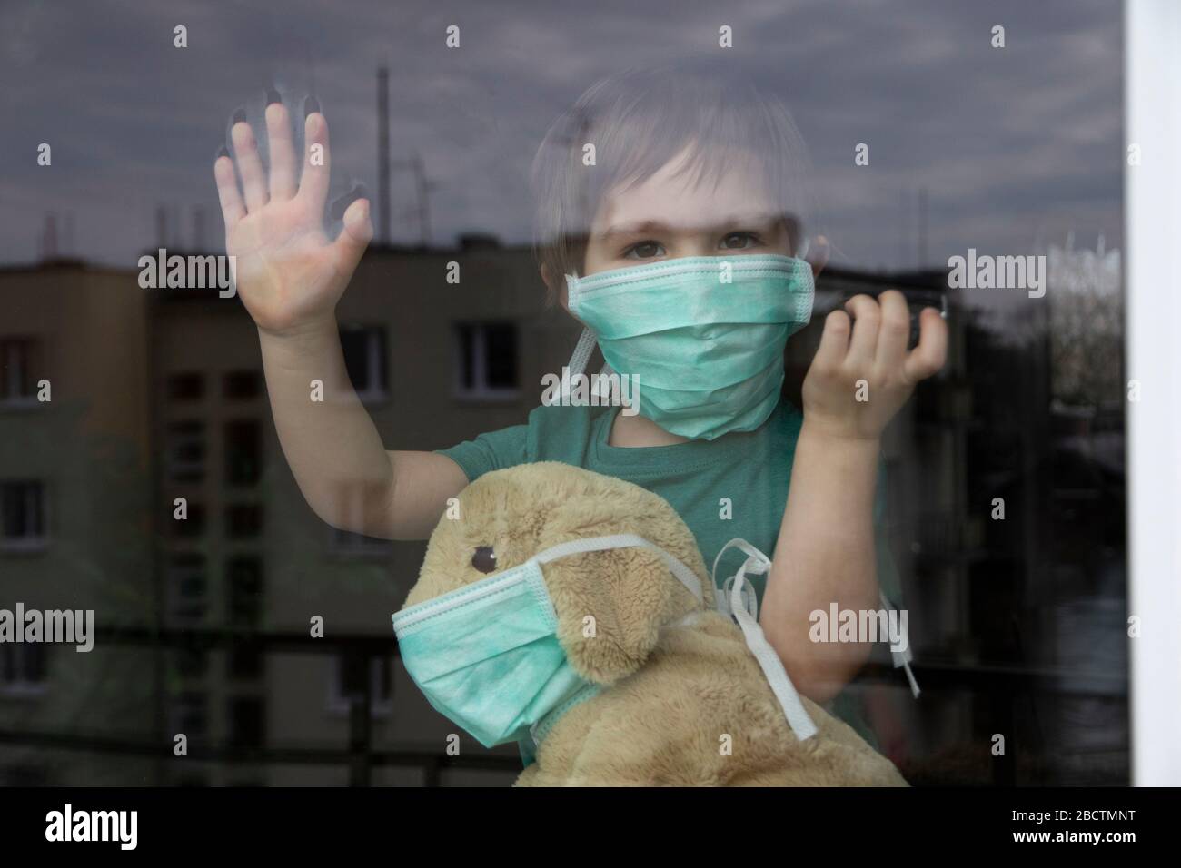 Coronavirus, Covid-19, Boy et son chiot farci dans des masques de protection regarder par la fenêtre, quarantaine à la maison Banque D'Images