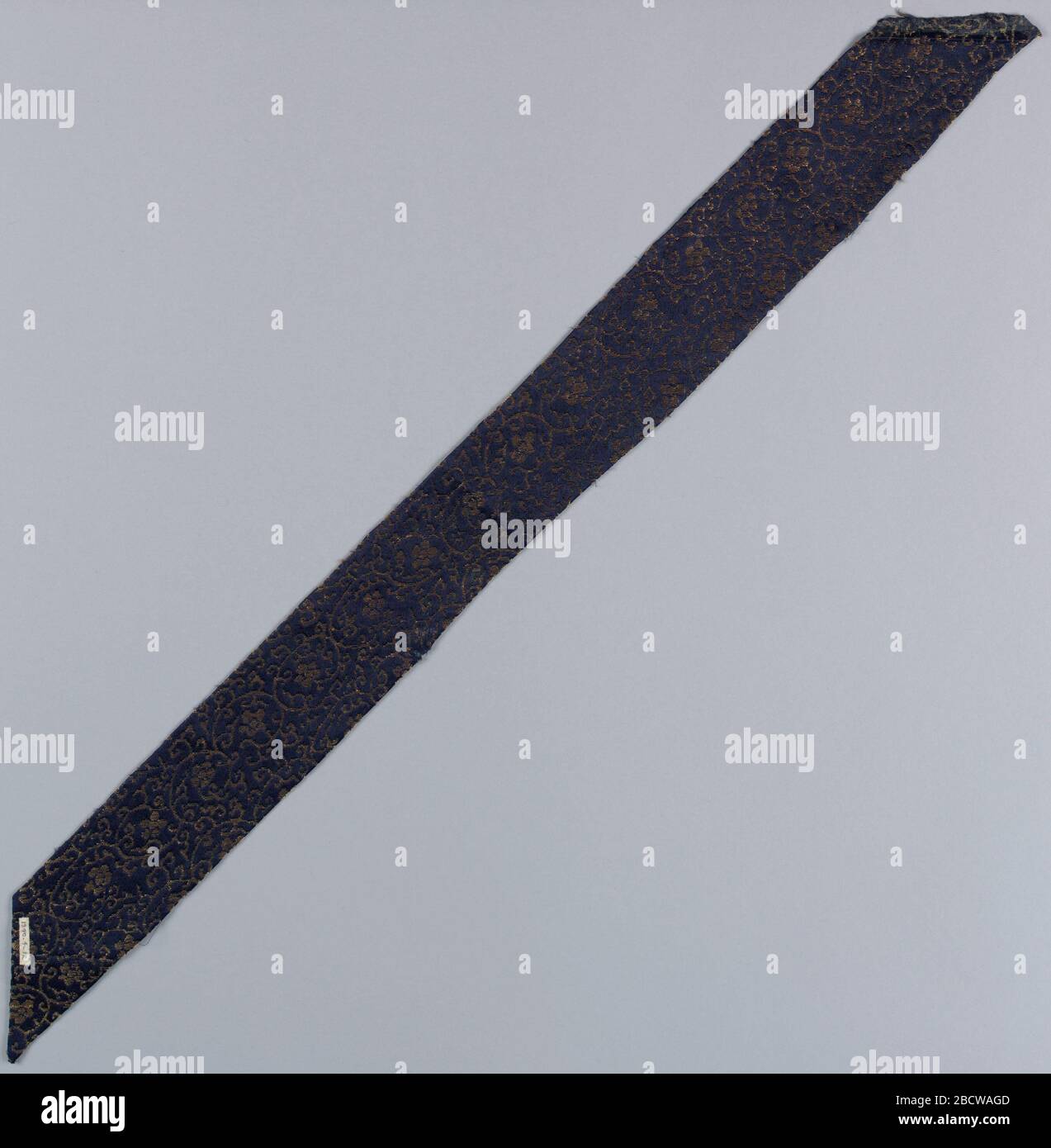 Textile. Recherche dans le sol de satin bleu ProgressDark avec une petite échelle, répétition de la vigne avec cinq pétales de fleurs, en or. Fragment coupé sur biais, bords retournés, comme si pour collier. Étoilé ou rigidifié au dos. Textile Banque D'Images