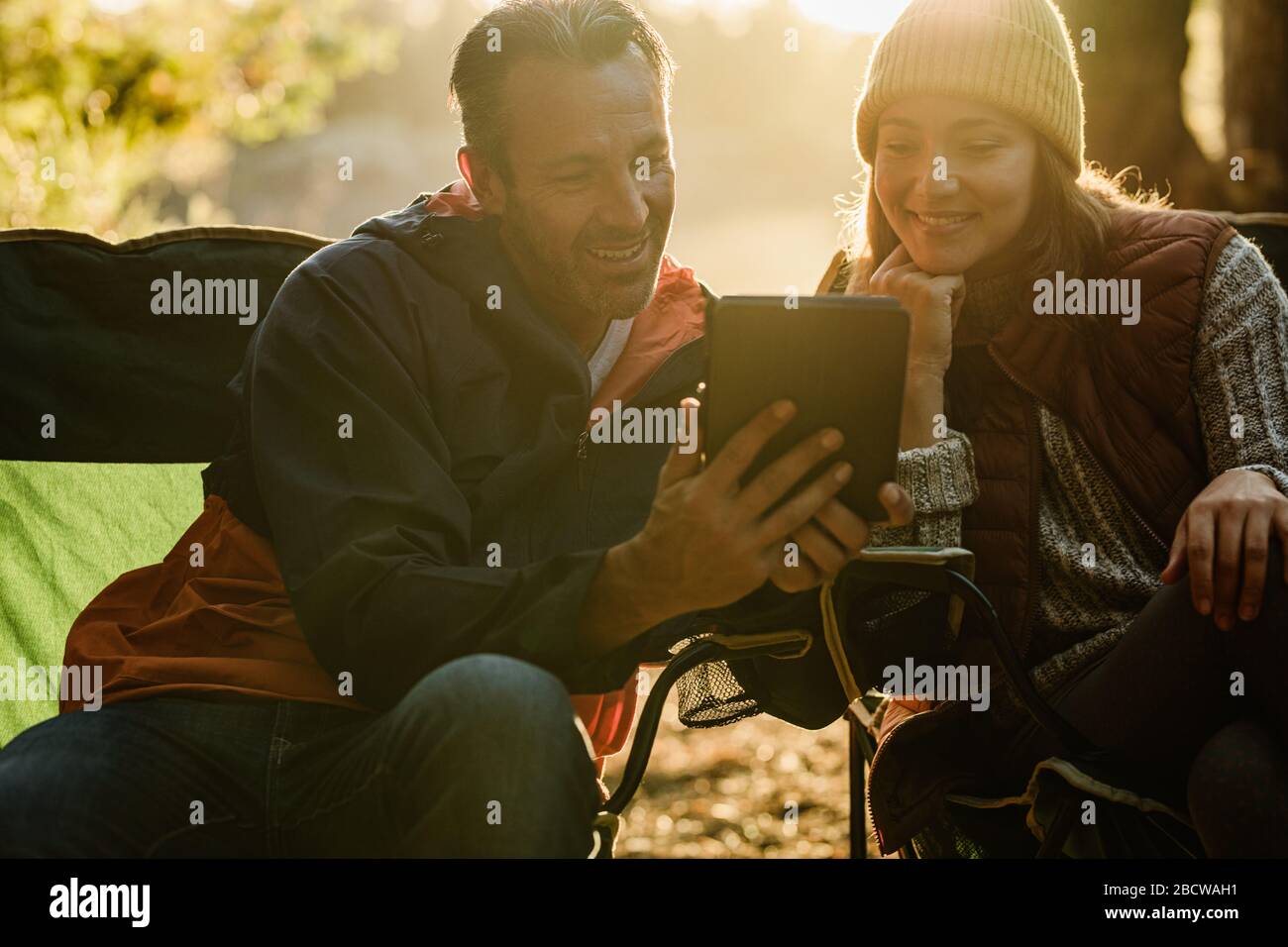 Homme souriant et femme se reposant à côté de la tente et utilisant une tablette numérique. Campeurs avec tablette numérique. Banque D'Images