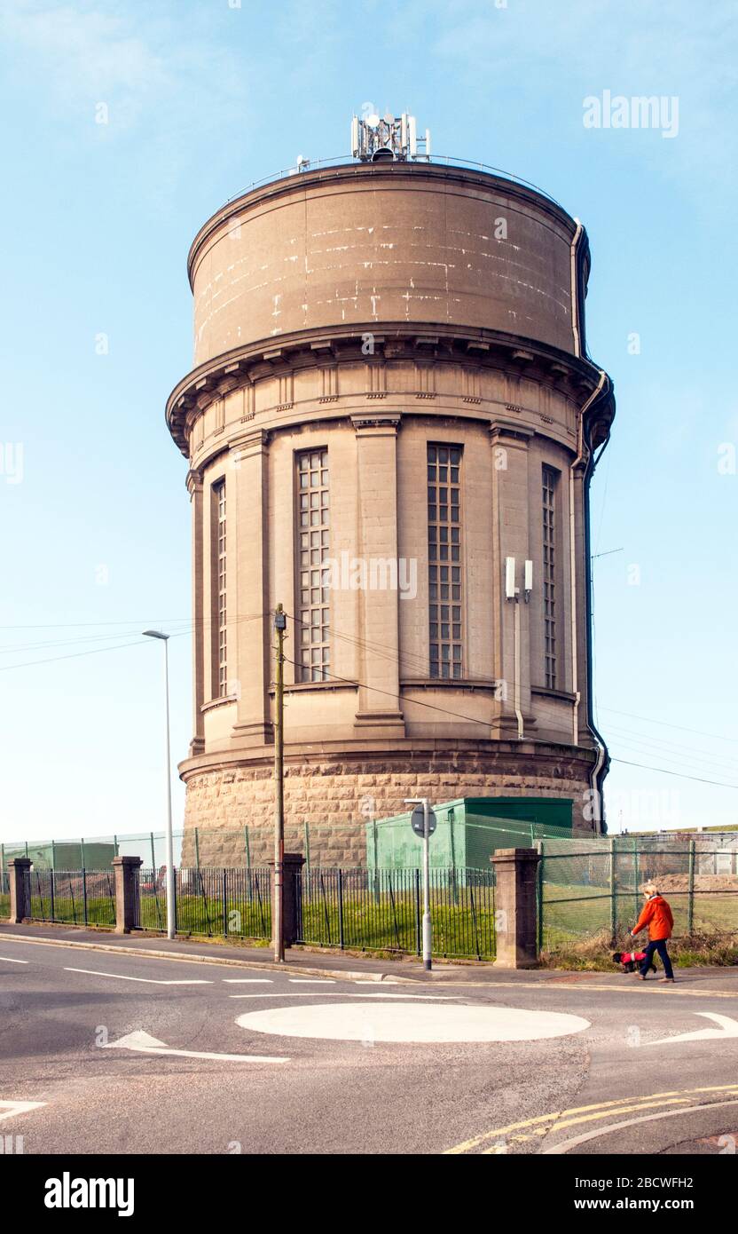 Lady in Red coat marchant son chien devant la Warbreck Water Tower qui fournit de l'eau aux ménages de Blackpool Lancashire Angleterre Royaume-Uni Banque D'Images