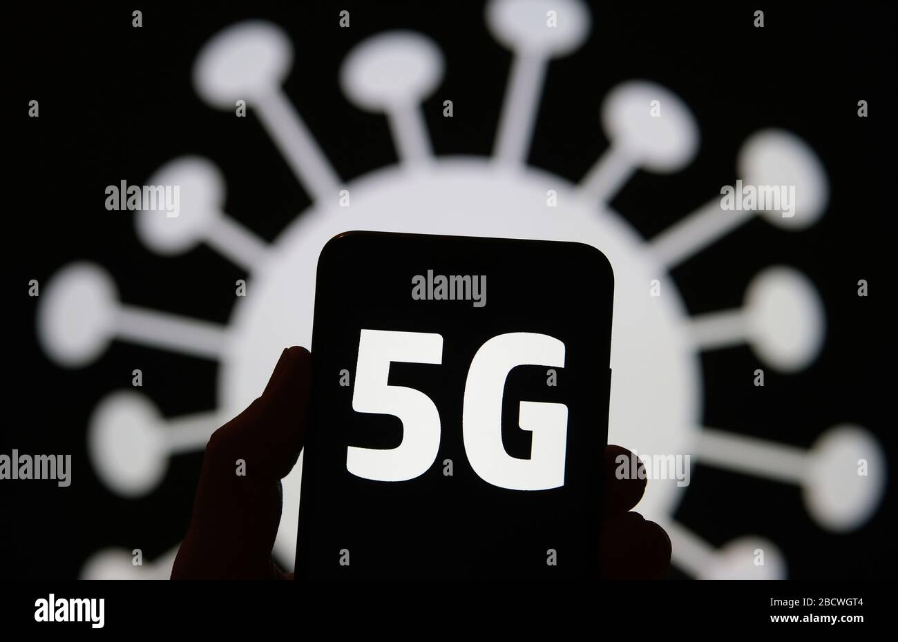 Rayonnement 5G en forme de COVID-19. Les lettres 5G sur la silhouette du smartphone tiennent dans une main et l'image du coronavirus se trouve en arrière-plan. Une vraie photo, pas un m Banque D'Images