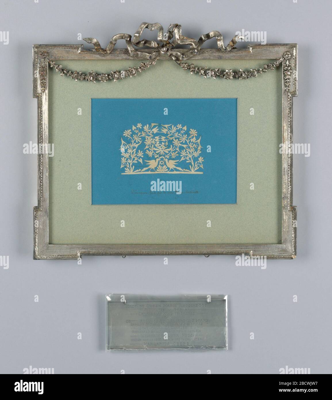 Motif fleuri avec oiseaux. Recherche dans le rectangle Progresshorizontal. Papier coupé au motif fleuri avec des oiseaux montés sur du papier bleu, sur lequel est une inscription, encadré dans un cadre en bois argenté sculpté. Motif fleuri avec oiseaux Banque D'Images