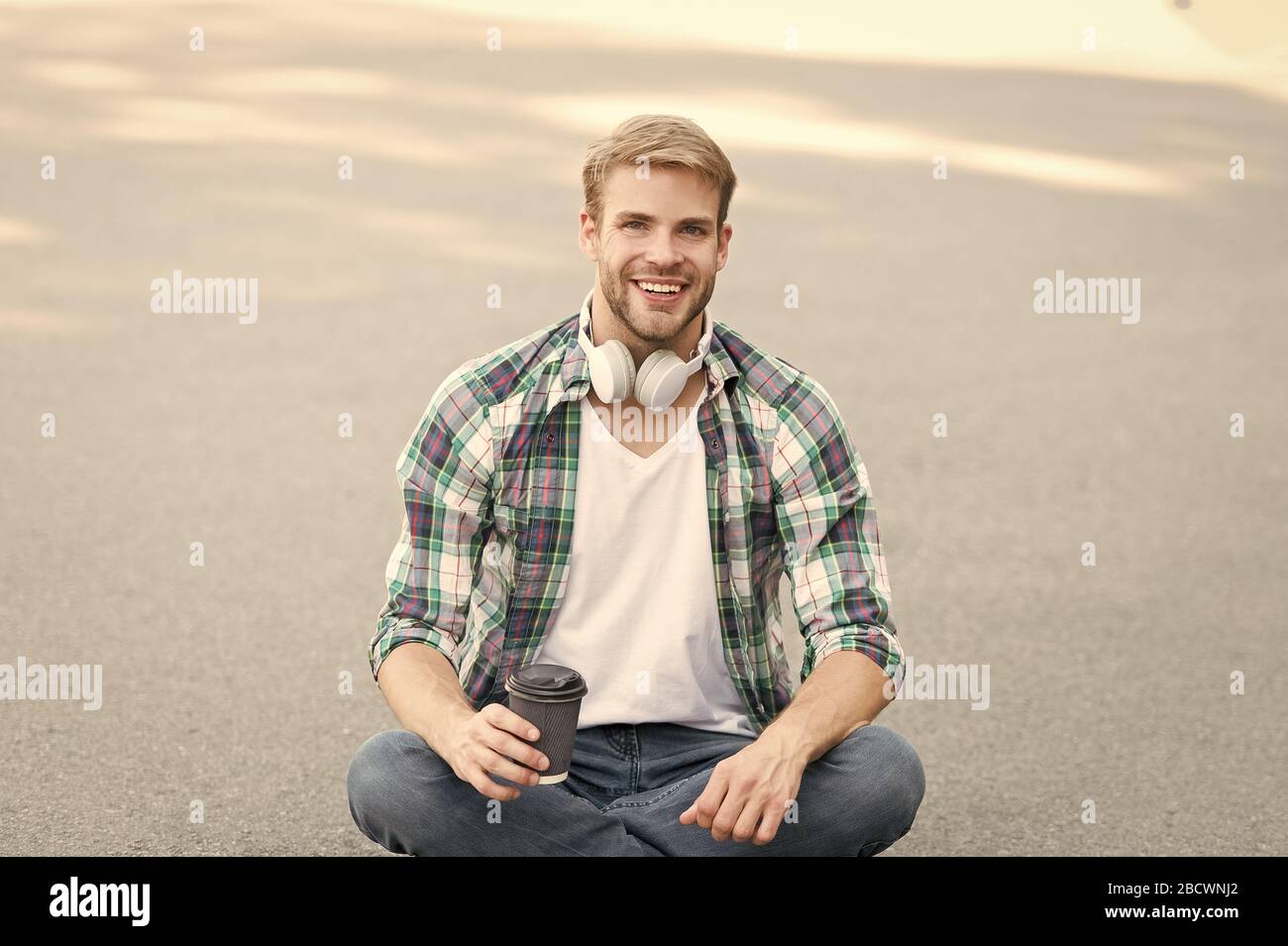 Être gai. chemise à carreaux homme étudiant. Se détendre et recharger. café d'aller. guy boire un café en plein air. L'homme s'asseoir sur le sol. étudiant insouciant en casque. l'éducation en ligne. écouter la musique. ebook concept. Banque D'Images