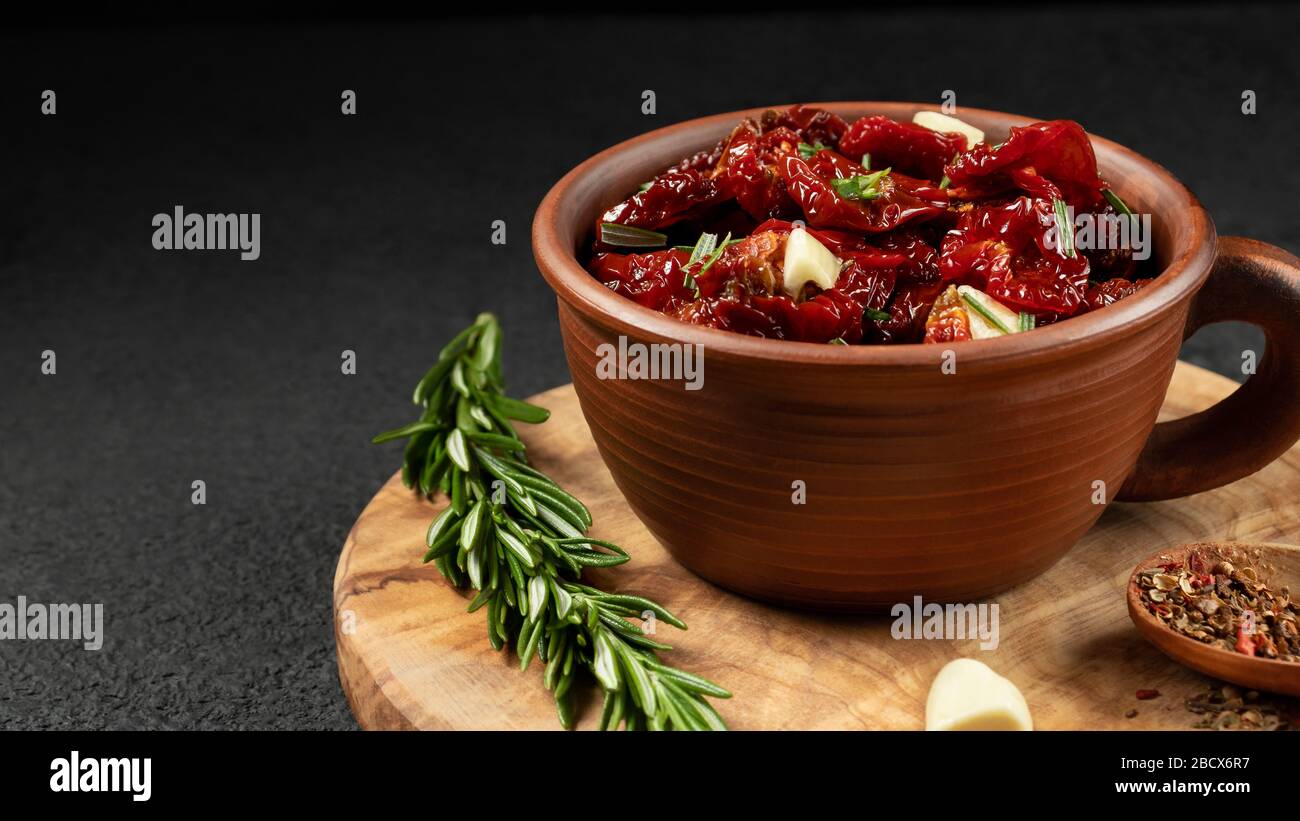 Tomates séchées au soleil avec ail, romarin et épices dans un bol en argile sur un tableau de découpe en bois d'olive, copyspace. Banque D'Images