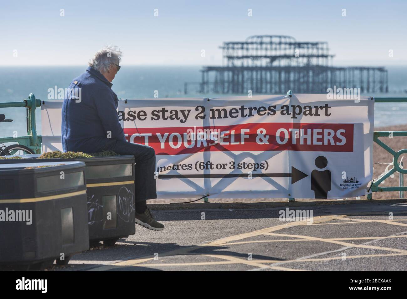 Pendant COVID-19. Un homme se trouve sur le panneau « Stay 2 mètres d'écart » en face des ruines de Brighton West Pier Banque D'Images