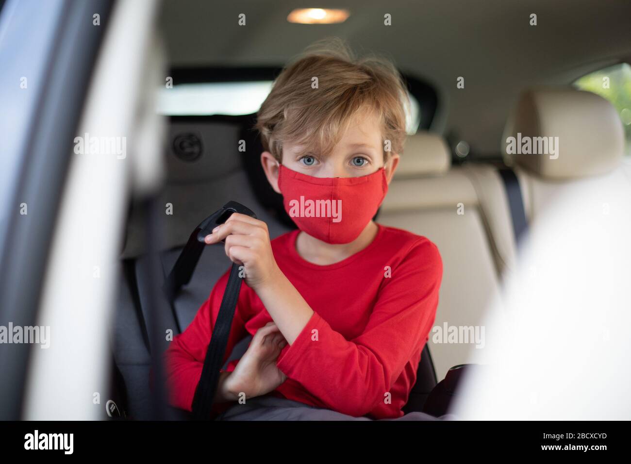 Un petit garçon sur le siège enfant de la voiture portant un masque facial. De nombreux pays recommandent aux citoyens de couvrir leurs visages pendant le coronavirus mondial Banque D'Images