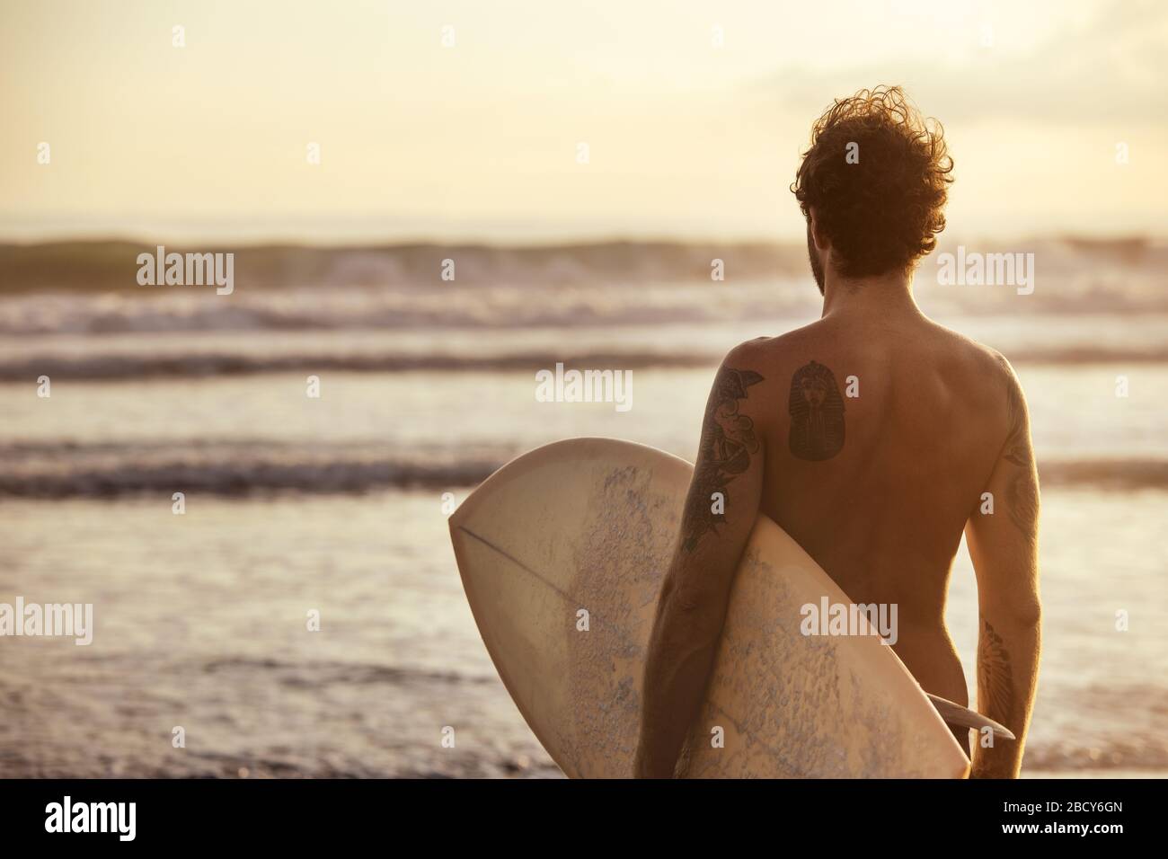 Un surfeur sportif est debout avec planche de surf blanche vierge à Sunset Ocean Beach Banque D'Images