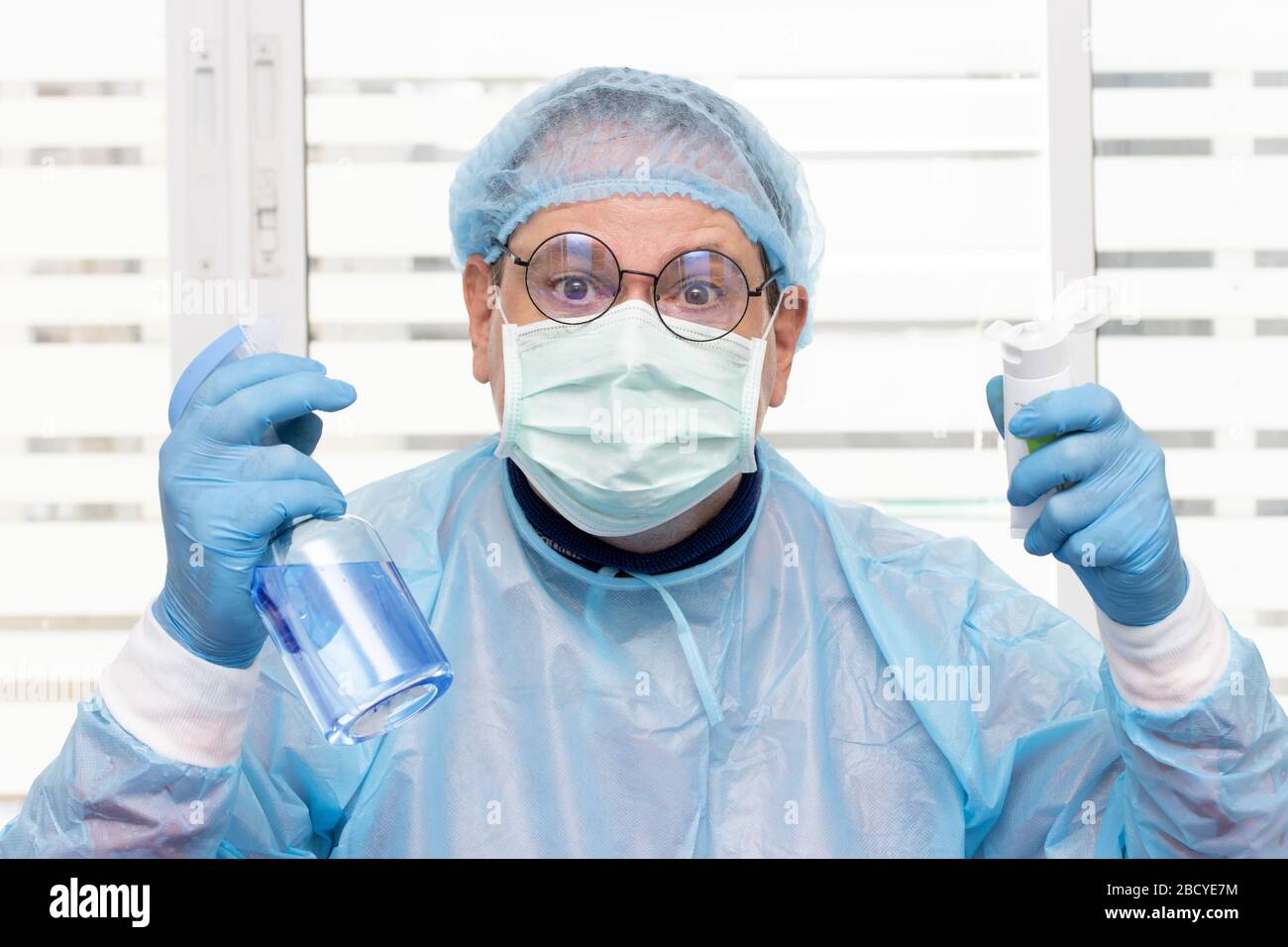 Médecin en costume de protection tenant une bouteille et un tube avec aérosol antibactérien et gel. Le personnel médical fait preuve d'un désinfectant. Banque D'Images