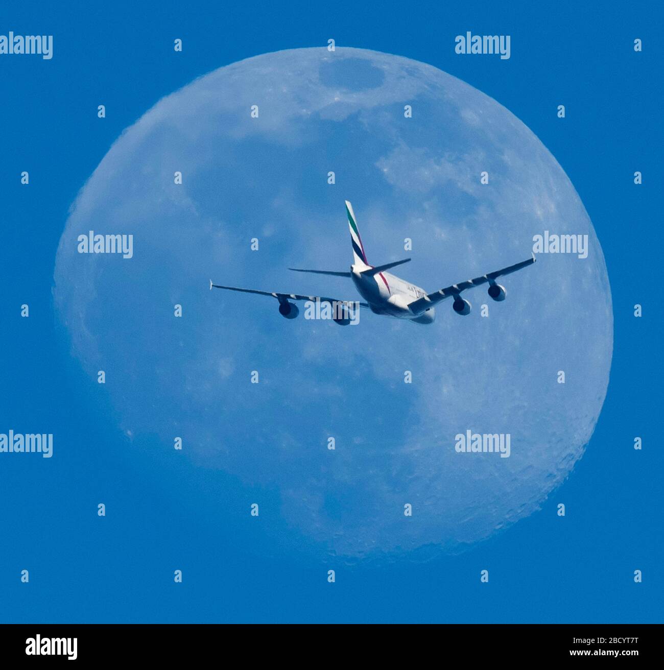 90 % de lune gibbale illuminée est traversée par un vol Emirates au départ de Londres Heathrow vers Dubaï dans un ciel bleu clair en début de soirée au-dessus de Londres, au Royaume-Uni. Crédit: Malcolm Park/Alay Banque D'Images