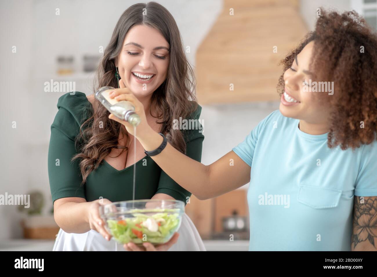Deux femmes ajoutent de l'huile de salade dans la salade de légumes. Banque D'Images