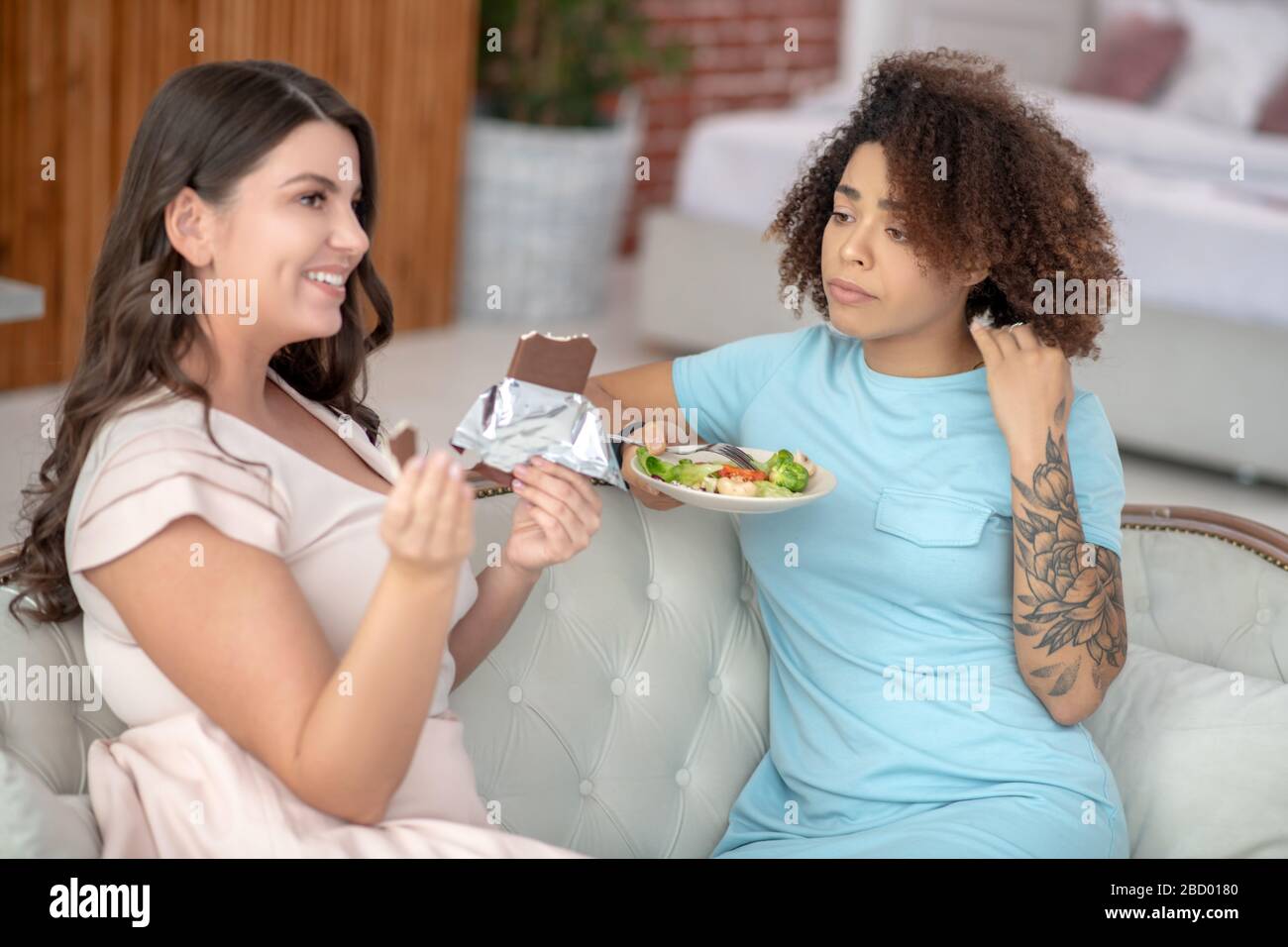 Femme triste avec salade de légumes et gaie avec un bar au chocolat. Banque D'Images