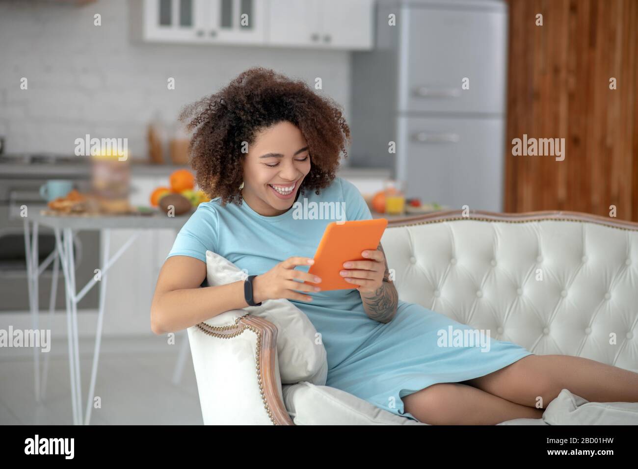 Jeune femme avec tablette inclinable sur un canapé à la maison. Banque D'Images